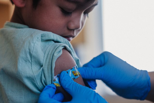 A healthcare provider applies a bandage to a young child's arm after receiving a vaccine shot